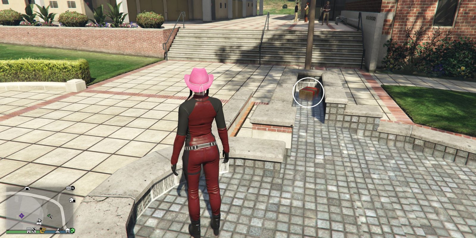 Image depicts a female player in GTA Online at the University of San Andreas stood inside the fountain in the main square of the campus. To the right, there is a small area on the side of the fountain that has a drain, and G's Cache is sat in there.