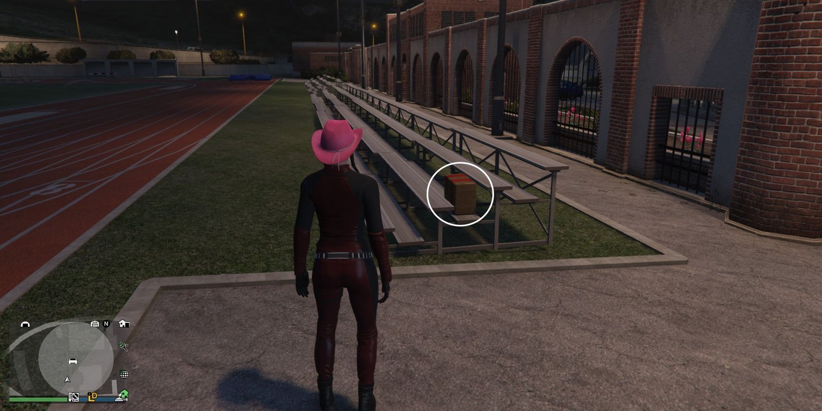 Image depicts a female player in GTA Online at the University of San Andreas on an athletic track. To the right of the track are some metal benches, and G's Cache is on the end of this row.