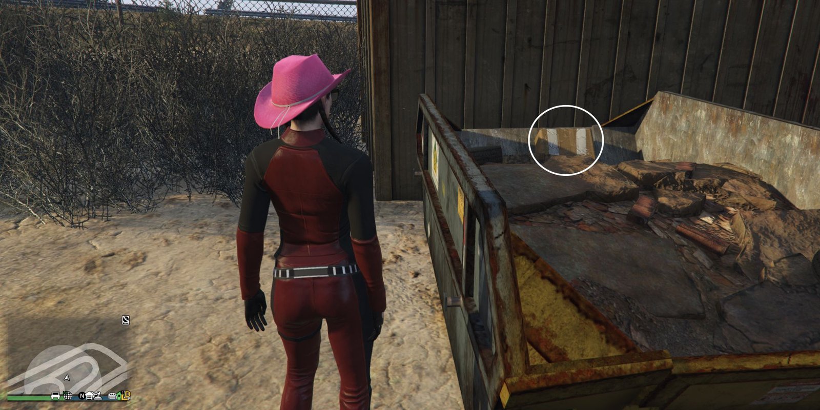 Image depicts a female player in GTA Online at Jay and Sons in El Burro Heights stood in front of a yellow skip container, which is next to a storage crate. At the back of the skip is G's Cache, among some rubbish.