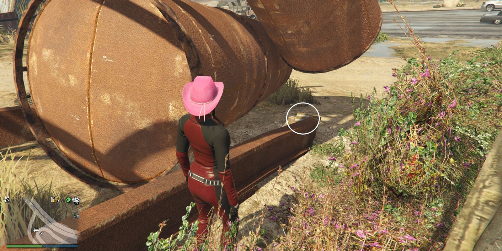 Image depicts a female player in GTA Online at Jay and Sons in El Burro Heights stood to the right of two copper tankers and some metal planks on the floor. Wedged in between the tankers and the plank on the floor, G's Cache is on the grassy area.