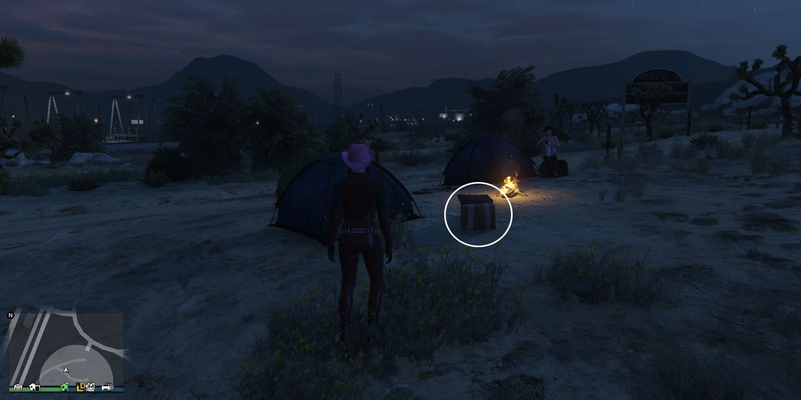 Image depicts a female character in GTA Online at Senora National Park stood in front of a campsite made up of two tents and a campfire. In the campsite, there are two cooler boxes on the floor next to the fire, and G's Cache is on the floor next to the one on the left.
