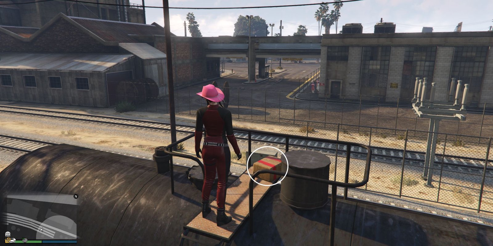 Image depicts a female character in GTA Online at Railyard Clucking Farms stood on top of a ladder for a black metal tanker on the railway tracks. At the top of the ladder, G's Cache box sits on the right-hand side.