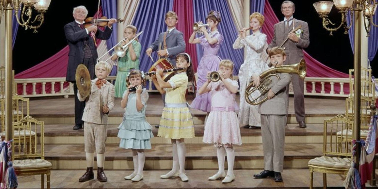 A group of musicians of all ages playing instruments in a theatre.